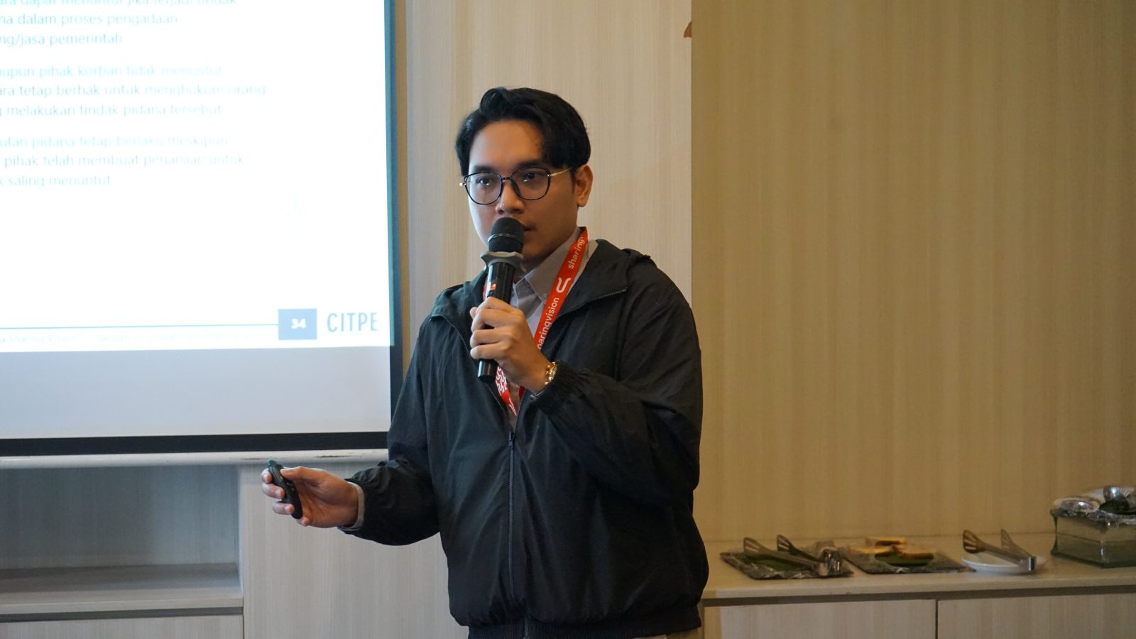 Faisal Sugangga presenting a CITPE session on procurement law, holding a microphone in front of a presentation screen
